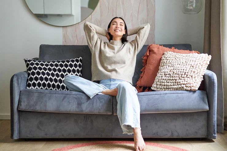 portrait of carefree asian woman enjoying dayoff sitting on sofa and smiling